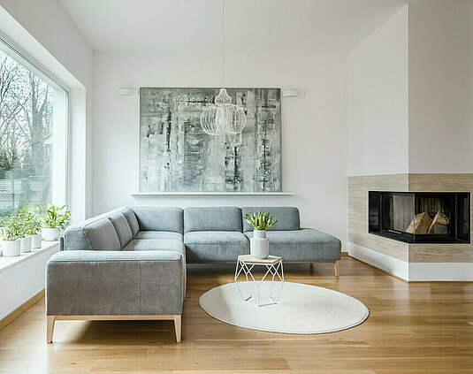 Geräumiges weißes Wohnzimmer mit grauer Eckcouch, großem modernem Gemälde und Kamin.